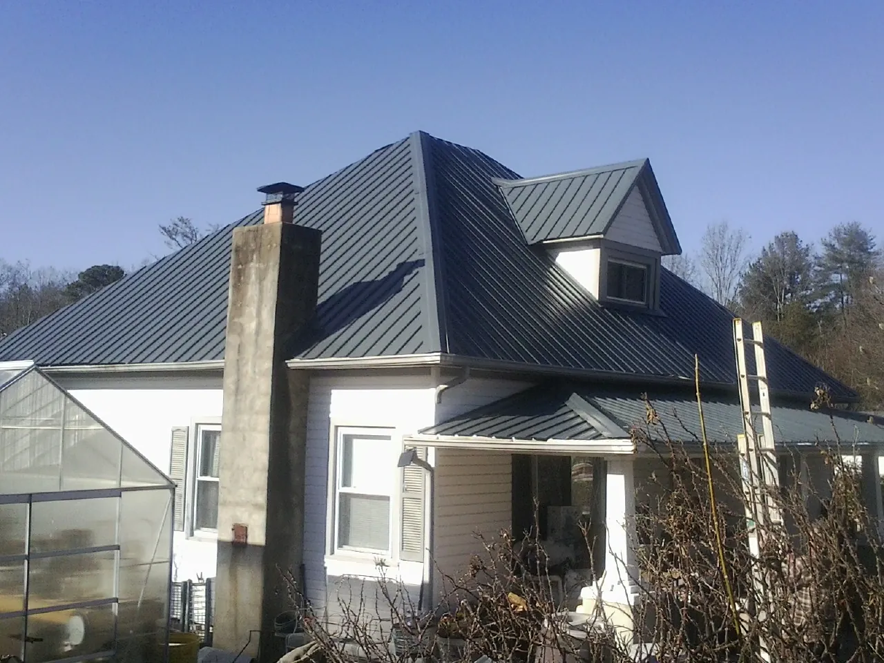 Dark blue standing seam metal roof on a white farmhouse with dormer — Slate & Tile Roof Repair by Roofing Brothers in Uniondale