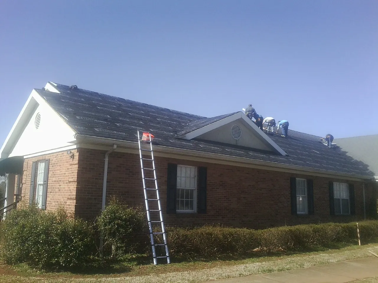 Crew tearing shingles off a brick ranch roof with a ladder set — Emergency Roof Repair work by our crew in Uniondale
