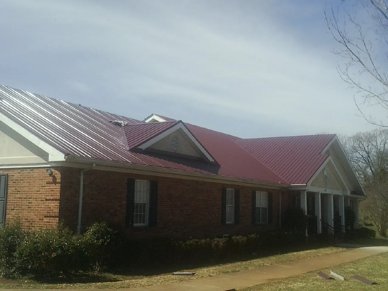 Red metal roof with gabled entries on a long brick building, from a Hail Damage Roof Repair job in Uniondale