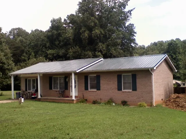 Gray metal roof on a brick ranch house with a side carport in Uniondale
