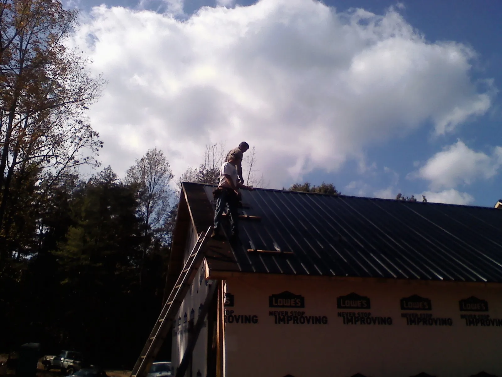 Roofer fastening dark metal panels high against a cloudy sky, from a Roof Inspection job in Uniondale