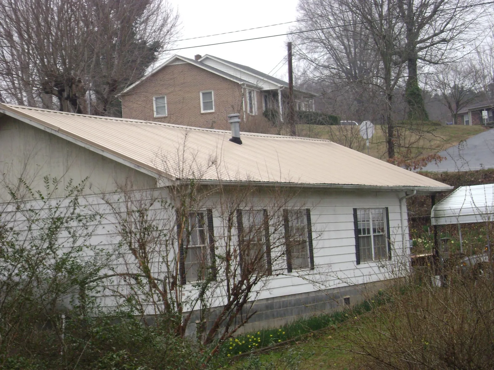Tan metal roof on a white sided house set into a hillside — Commercial Roofing by Roofing Brothers in Uniondale