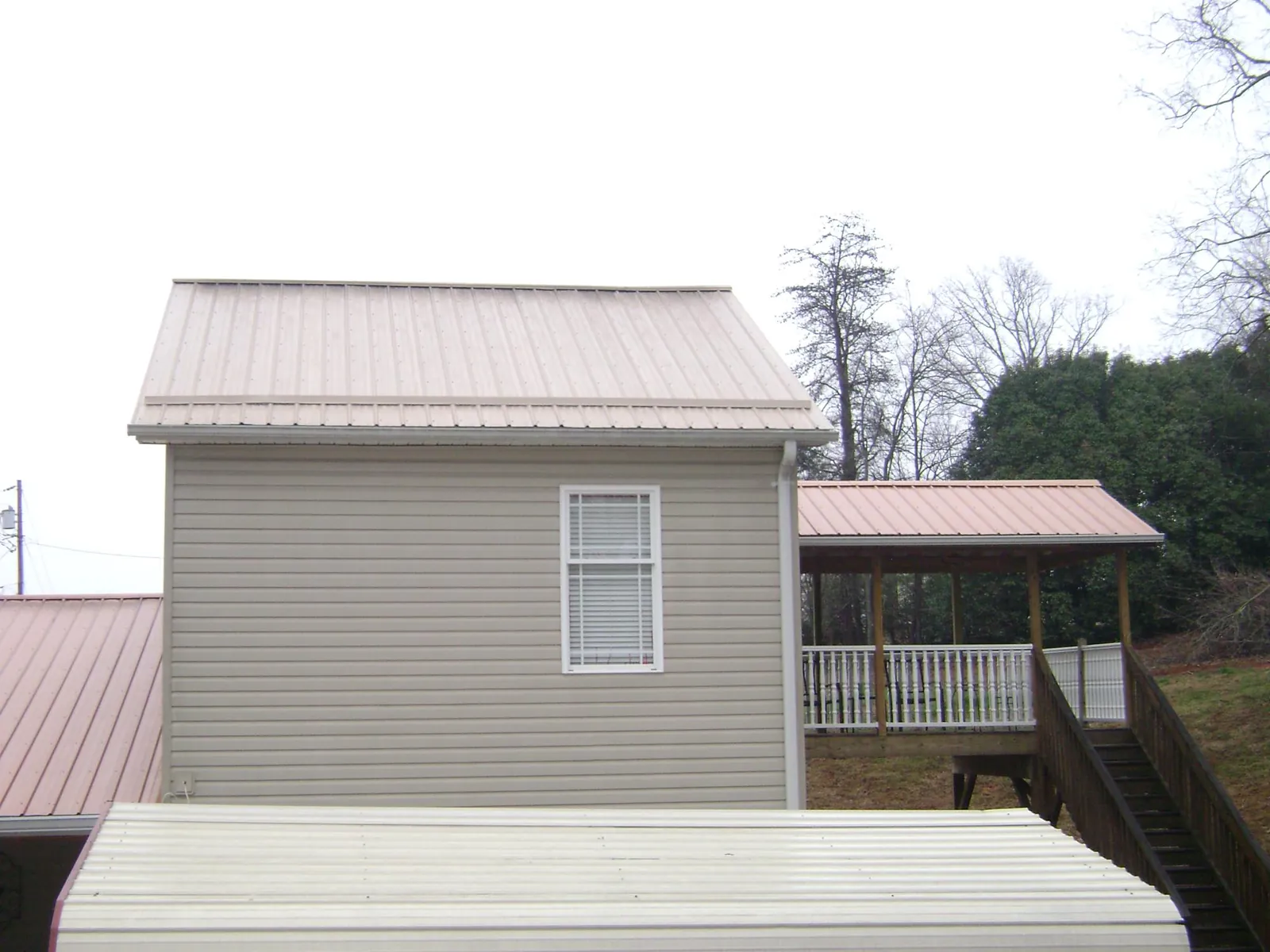 Tan metal roofs on a two story addition and attached porch, from a Roof Replacement job in Uniondale
